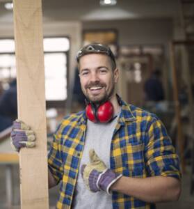 Smiling carpenter holding wood in the workshop